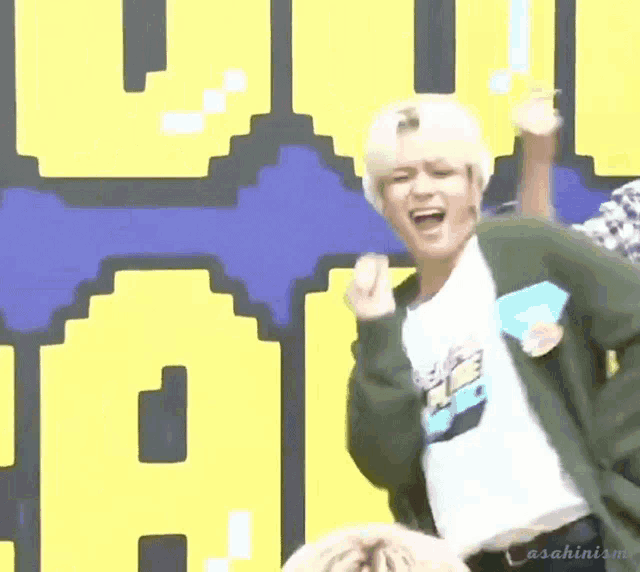 a man wearing a green cardigan and a white t-shirt is dancing in front of a pixelated wall .