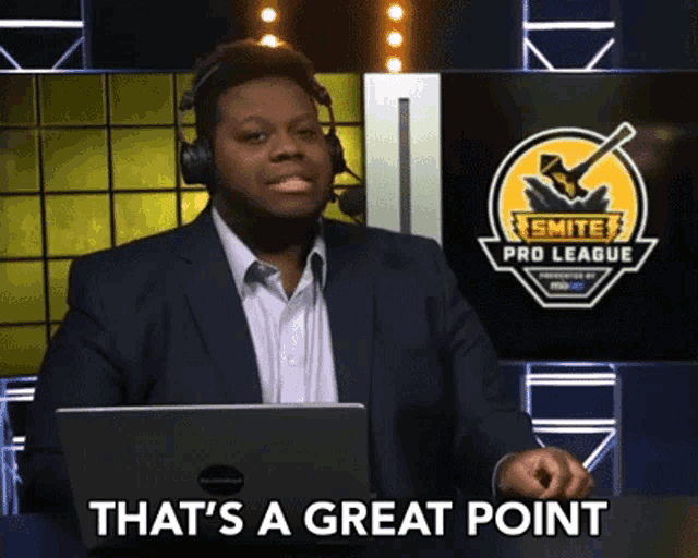 a man in a suit and headphones says that 's a great point in front of a smite pro league sign