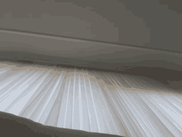 a close up of a white pleated curtain with a window in the background