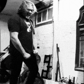 a man in a black shirt is standing in a room with a ladder in the background