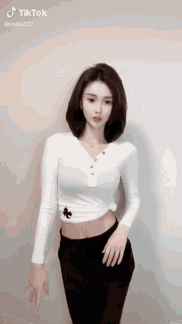 a woman in a white shirt and black pants is standing in front of a wall .