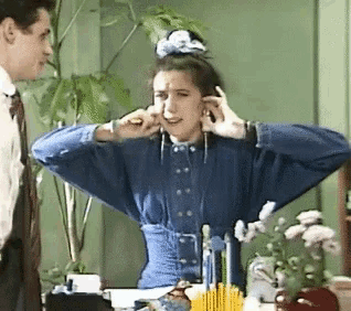 a woman in a blue shirt is covering her ears while a man looks on .