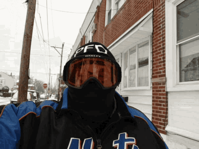 a man wearing oakley goggles stands in front of a red brick building