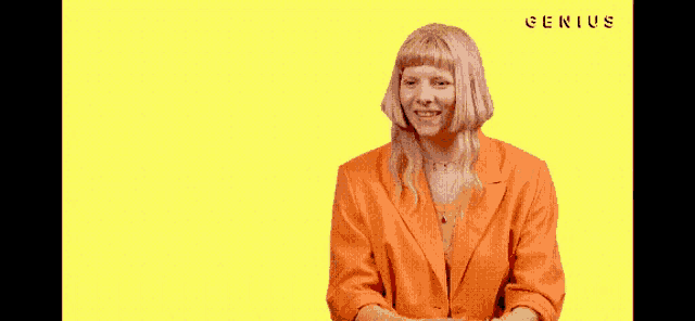 a woman in an orange jacket is making a peace sign with her hands .