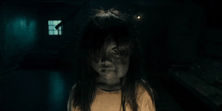 a little girl with long hair is standing in a dark room .