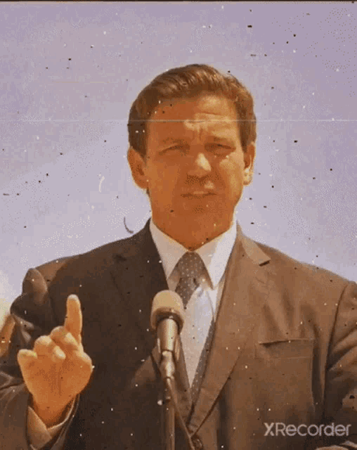 a man in a suit and tie is giving the middle finger in front of a microphone