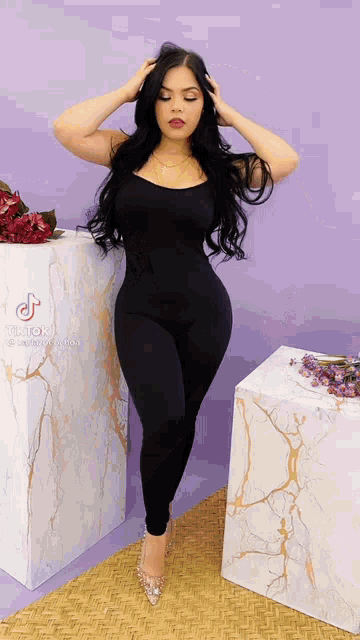 a woman in a black jumpsuit is standing in front of marble blocks