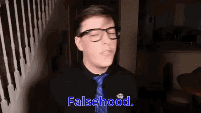 a man wearing glasses and a tie is standing in a dark room and saying `` falsehood '' .