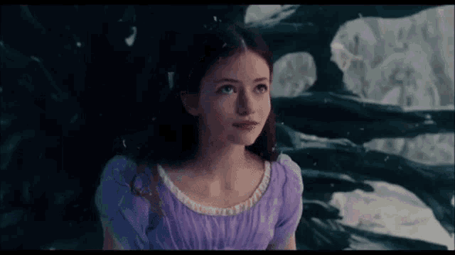 a young woman in a purple dress is standing in front of a wall .