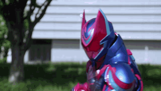 a person in a red and blue armor is standing in front of a tree .