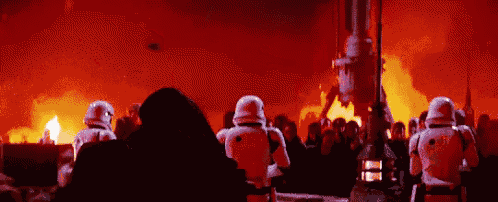 a group of stormtroopers are standing in front of a burning building in a star wars movie .