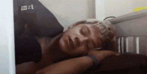 a man is sleeping in a crib with his eyes closed and his head on a pillow .