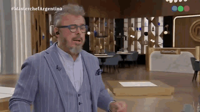 a man in a suit and glasses is standing in front of a masterchef sign