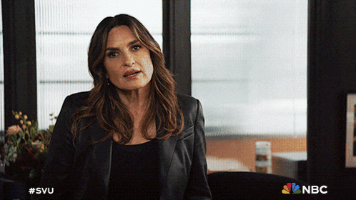 a woman in a black leather jacket is sitting in front of a window with the nbc logo in the corner