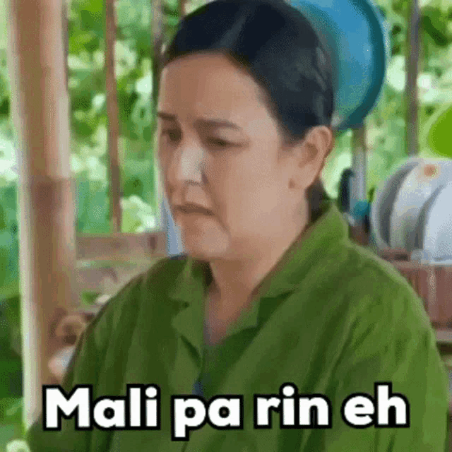 a woman in a green shirt is making a funny face with the words mali pa rin eh on her face .