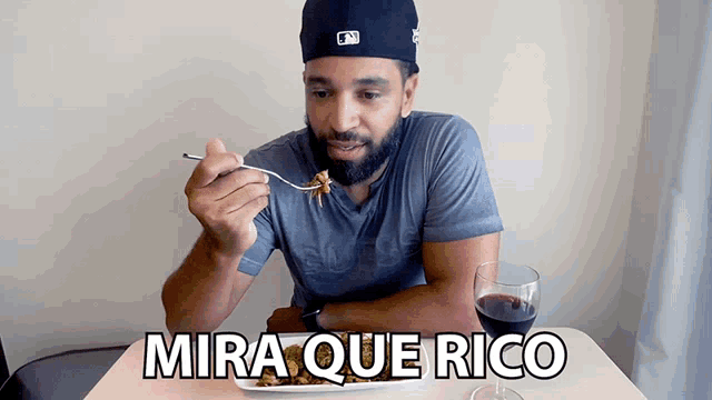 a man is sitting at a table with a plate of food and a glass of wine with mira que rico written on it
