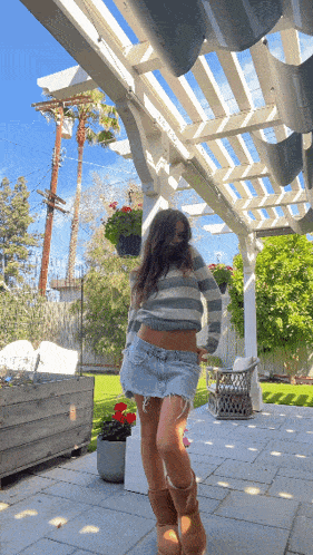 a woman in a striped sweater and denim skirt is standing under a white pergola