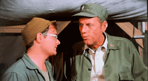 two men in military uniforms are talking and one has a skull on his hat