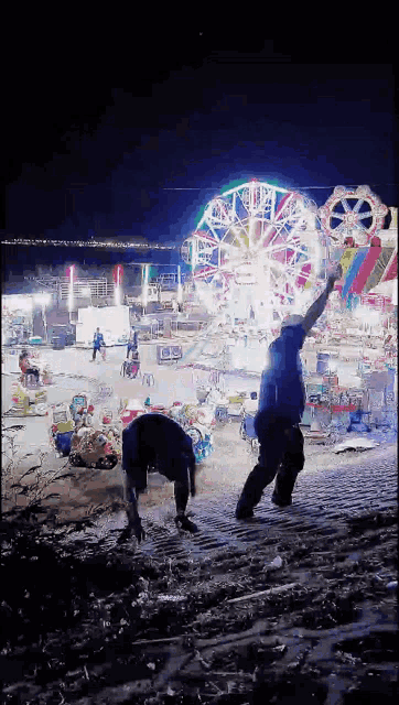 a man stands in front of a ferris wheel at an amusement park at night