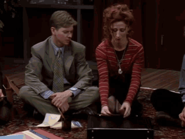 a man in a suit sits next to a woman in a red sweater