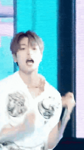 a young man in a white shirt is standing in front of a microphone and making a funny face .