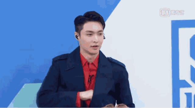 a man in a suit and red shirt is standing in front of a blue wall