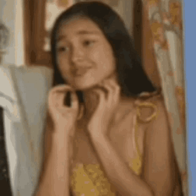 a woman in a yellow dress is holding her hands to her face while looking at the camera .