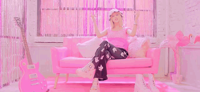 a woman is sitting on a pink couch with a pink guitar in the background .