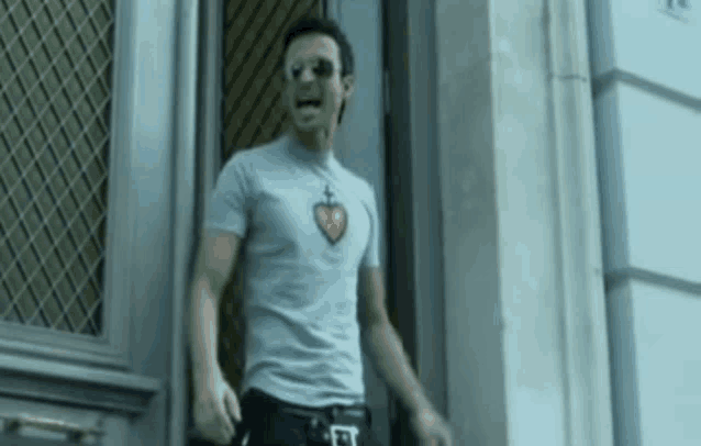 a man wearing sunglasses and a t-shirt with a heart on it is walking out of a doorway .