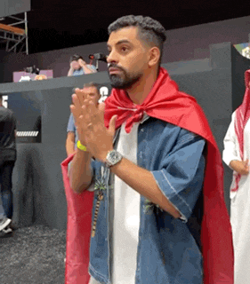 a man wearing a red cape is clapping his hands while standing in front of a crowd .