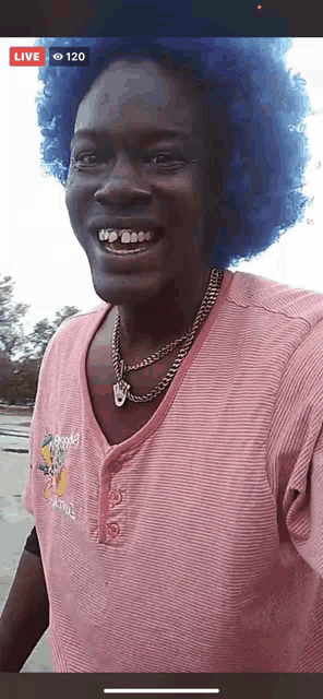 a man with blue hair and a pink shirt is smiling