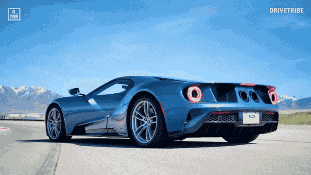 a blue sports car is driving down a road with mountains in the background