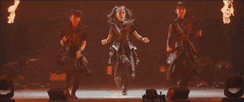 a group of girls are dancing on a stage with fire in the background