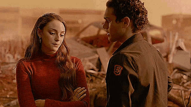 a man and a woman are standing next to each other and looking at each other in front of a pile of junk .