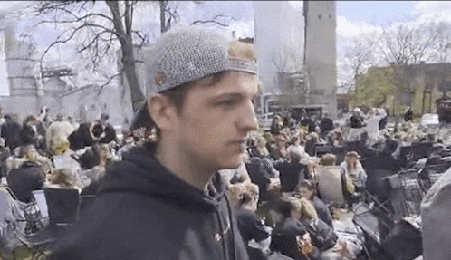 a man wearing a hat is standing in a crowd of people .