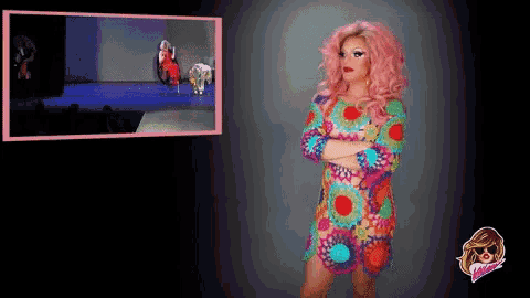 a woman with pink hair is standing with her arms crossed in front of a tv screen