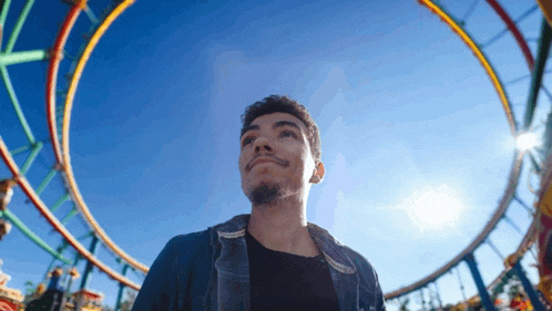 a young man is standing in front of a roller coaster at an amusement park