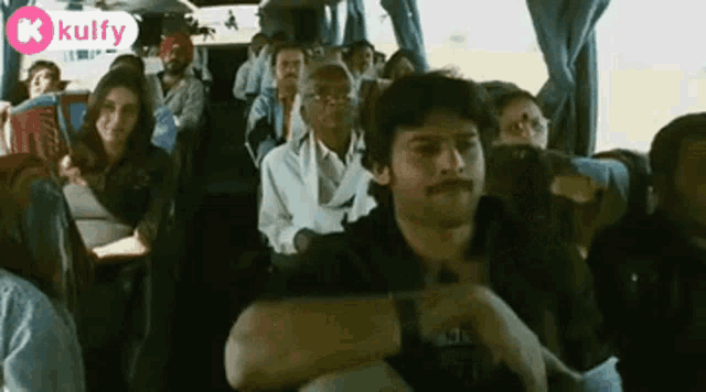 a man with a mustache is sitting on a bus with a crowd of people .