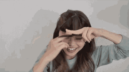 a woman is smiling and making a funny face while holding her hair in front of her face .