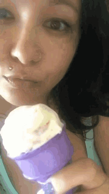a woman is eating an ice cream cone with a purple cap .