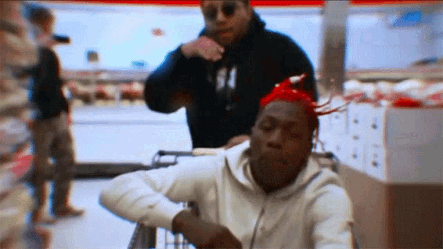 a man wearing a red headband is pushing another man in a shopping cart in a store