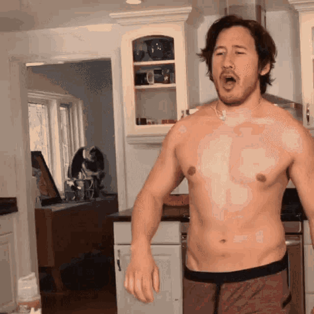 a shirtless man stands in a kitchen with his mouth wide open