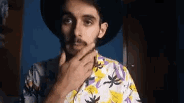 a man with a beard wearing a hat and a colorful shirt is adjusting his tie .