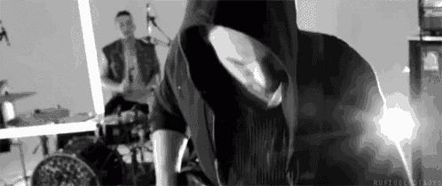 a man in a hoodie is standing in front of a drum set in a room .