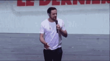a man in a white shirt is holding a microphone while standing in front of a wall .