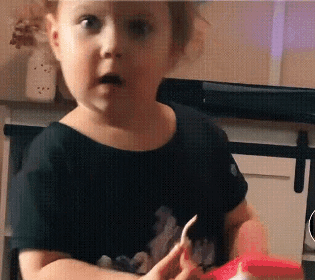 a little girl in a black shirt is holding a piece of paper