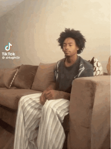 a man is sitting on a couch with his legs crossed and looking at the camera .