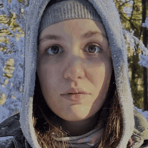 a woman wearing a hooded jacket and a hat looks at the camera