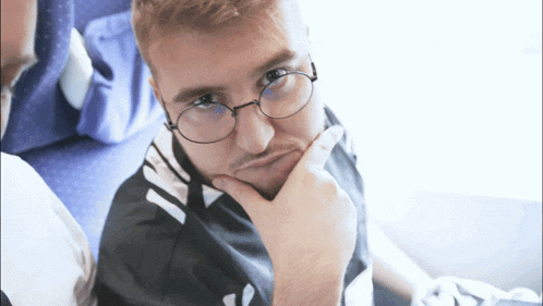 a man wearing glasses and a black and white shirt has his hand on his chin
