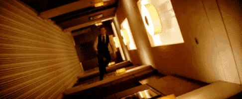 a man in a suit and tie is walking down a hallway with a light on the wall